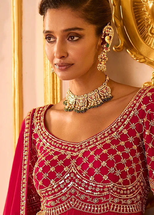 Close-up of a woman wearing an ornate deep red embroidered traditional anarkali suit outfit with intricate gold beadwork and jewelry.