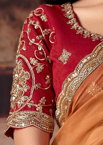 Close-up of a traditional Indian saree blouse in deep red with intricate gold embroidery designs and mirror work, paired with a peach-orange colored drape.