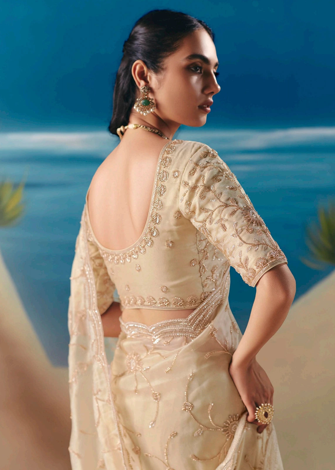 Sheer cream organza tissue silk fabric saree with deep blouse back design featuring artisanal beadwork and golden sequins embroidery work done by hand.