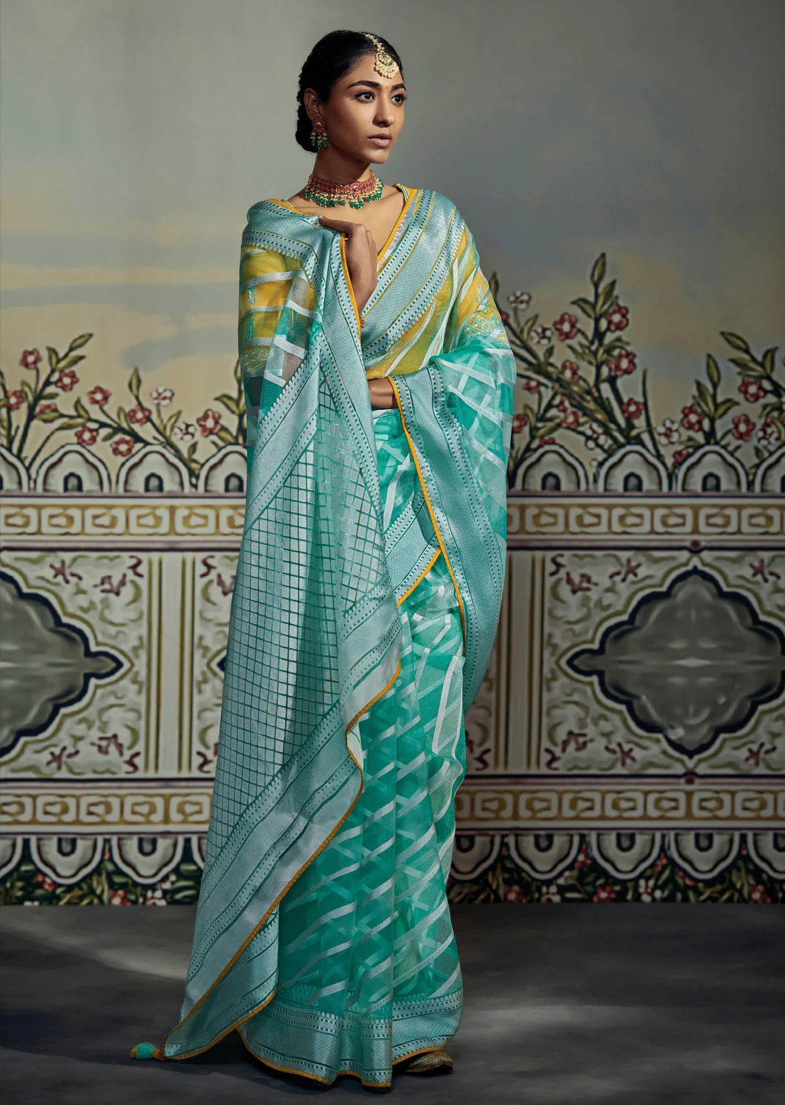 woman standing in soft brasso silk turquoise blue saree and yellow blouse