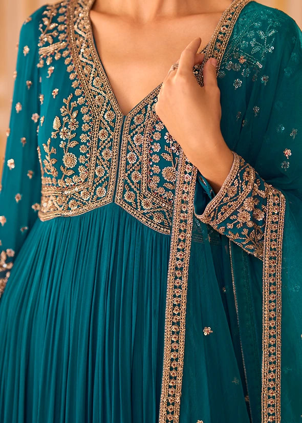 Close-up of a teal blue traditional anarkali with intricate gold and silver sequins embroidery, featuring a deep V-neckline, pleated skirt, and matching embroidered dupatta.