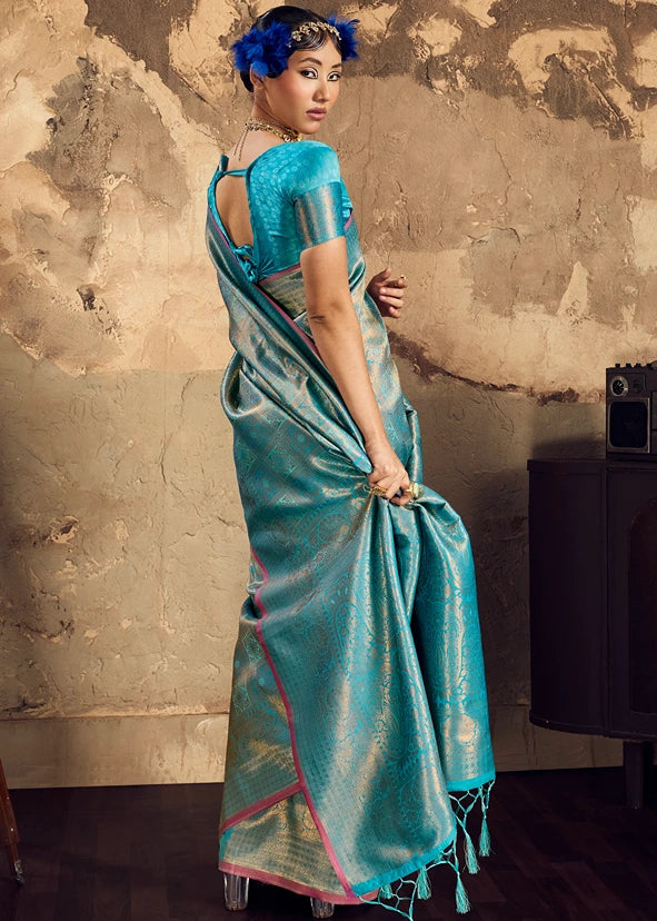 Woman wearing a turquoise blue and gold zari Banarasi saree with pink border accents and traditional Indian jewelry.