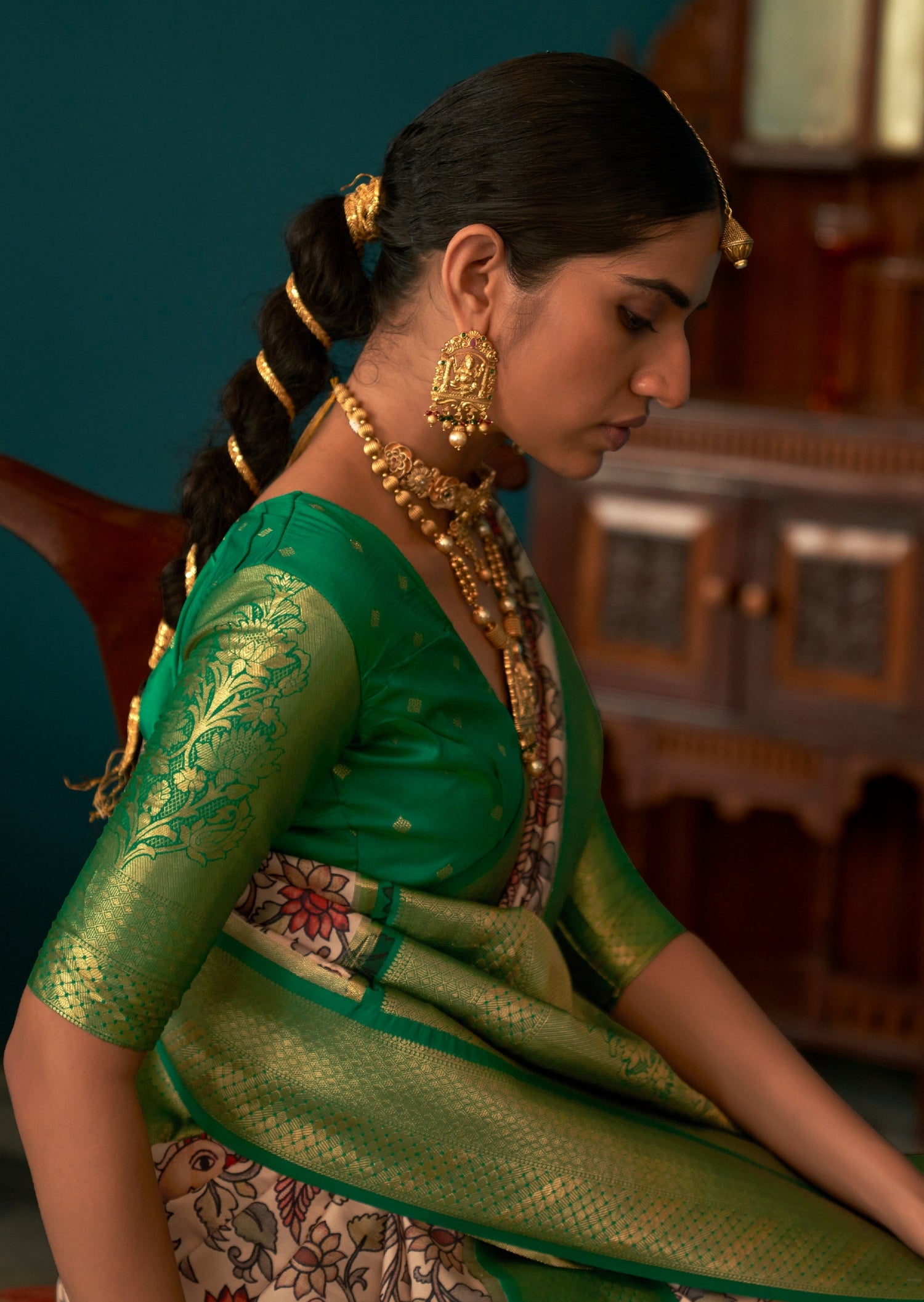 Side profile picture of woman sitting in green Banarasi zari saree