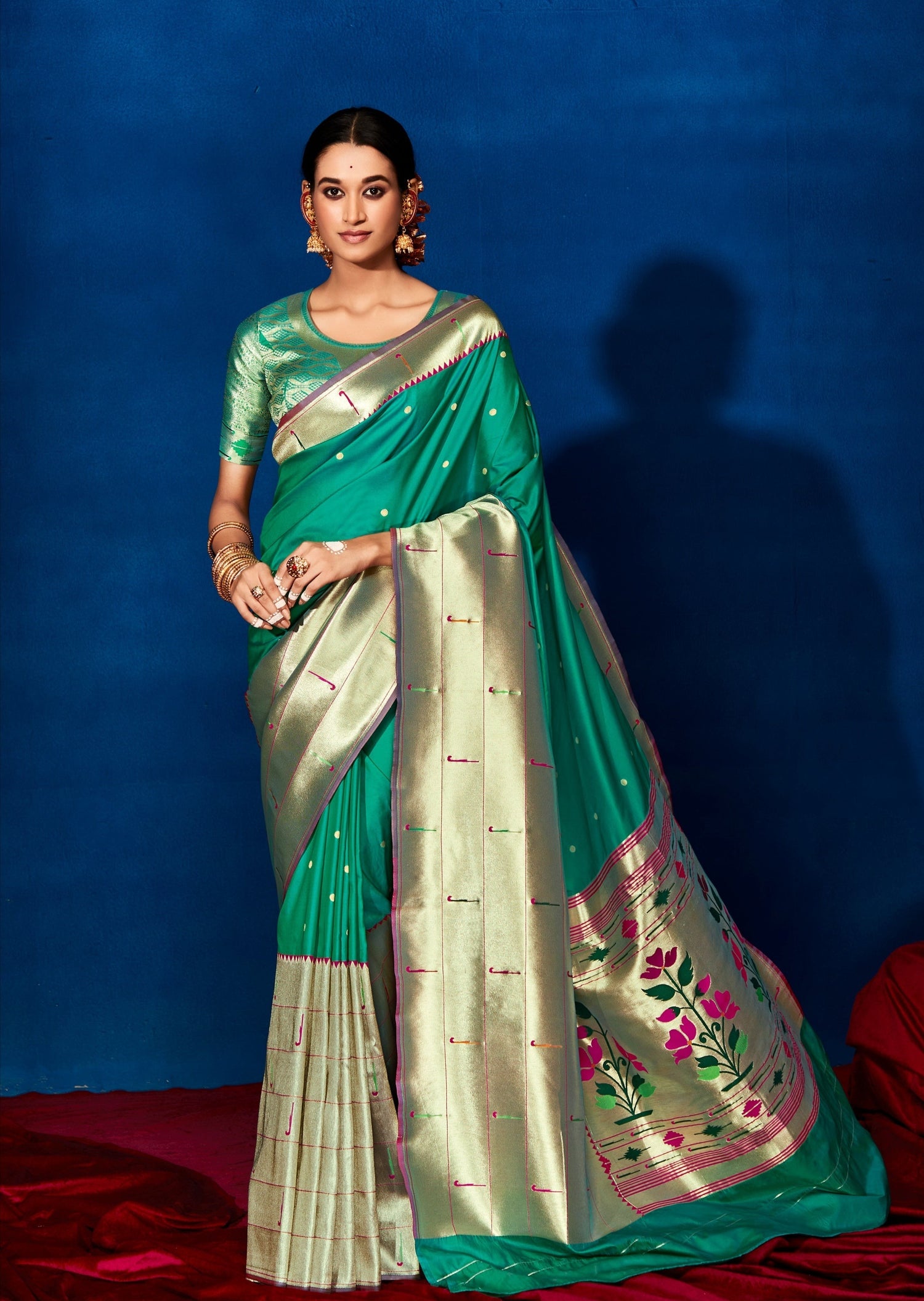 Woman in Green silk saree standing in front of blue wall