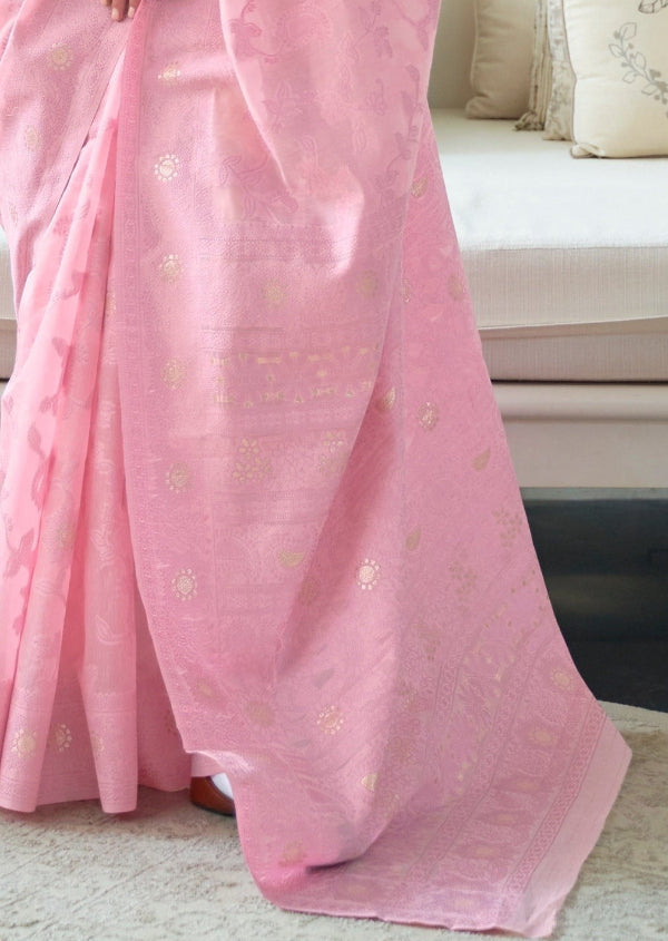 A close-up of a light pink saree with delicate gold floral lucknowi motifs and a gold border, draped elegantly on a woman in an indoor setting.